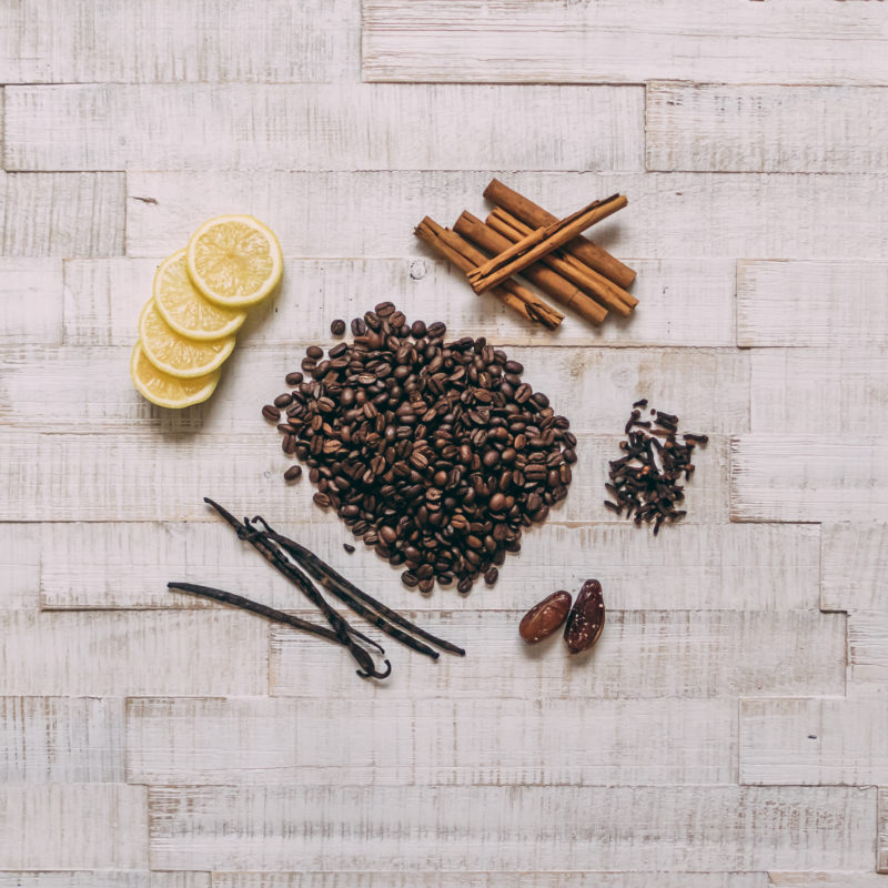 Auf dem Bild sind die Zutaten für fünf verschiedene Cold Brew Coffees zu sehen. Neben Kaffeebohnen sind Gewürze und Zitronenscheiben zu sehen.
