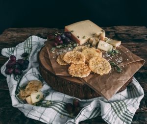 Käsechips auf Holzbrett mit frischen Trauben, Parmesankäse und Gauda am Stück