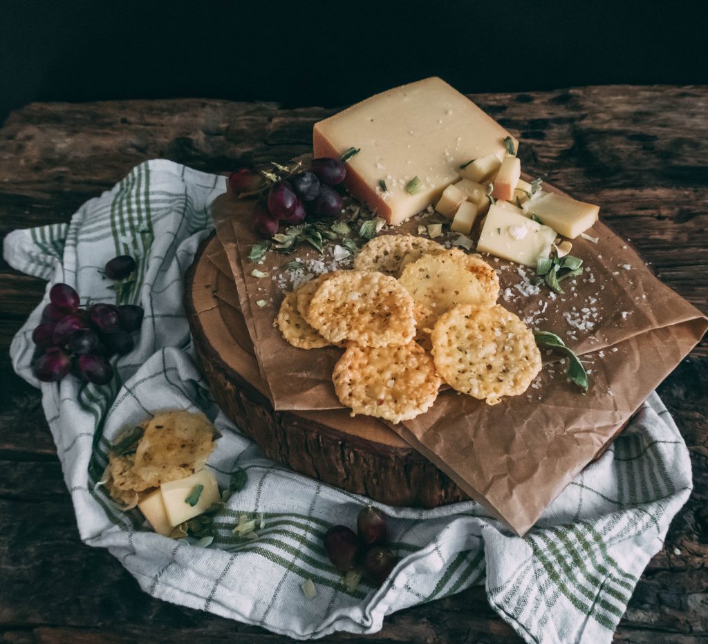 Käsechips auf Holzbrett mit frischen Trauben, Parmesankäse und Gauda am Stück