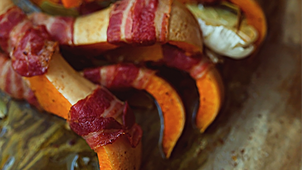 Auf einem Backblech liegen Kürbisspalten im Speckmantel.