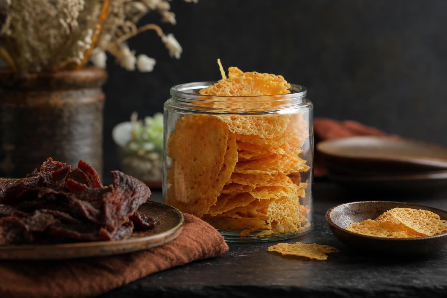 Airfryer Käsechips – Ein Glas mit gestapelten, goldgelben Käsechips steht auf einer Küchenarbeitsplatte im weichen Tageslicht.