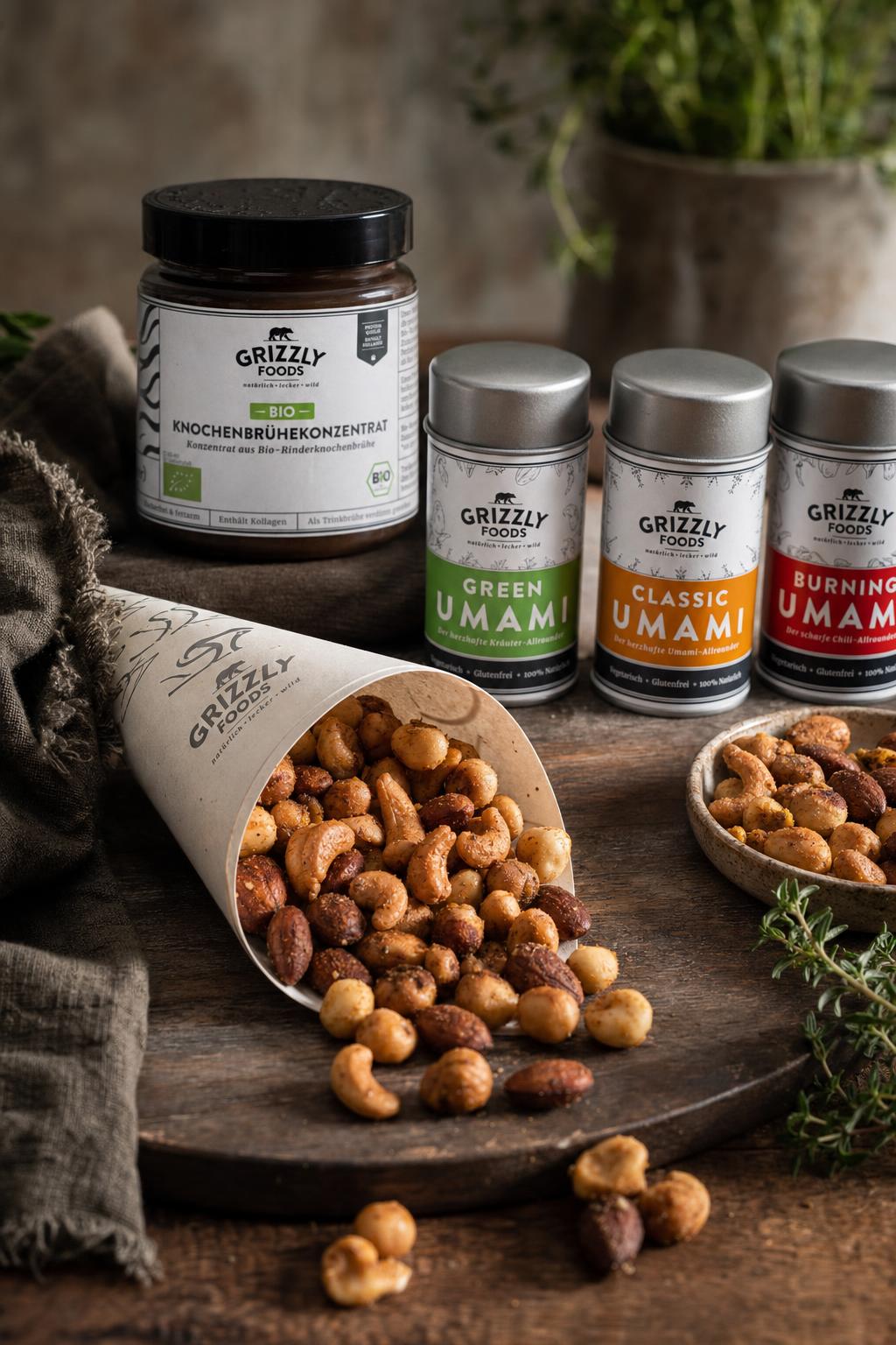 Hand hält eine Papiertüte mit gerösteten Cashews, Haselnüssen und Mandeln, im Hintergrund weitere Nüsse auf Holz.