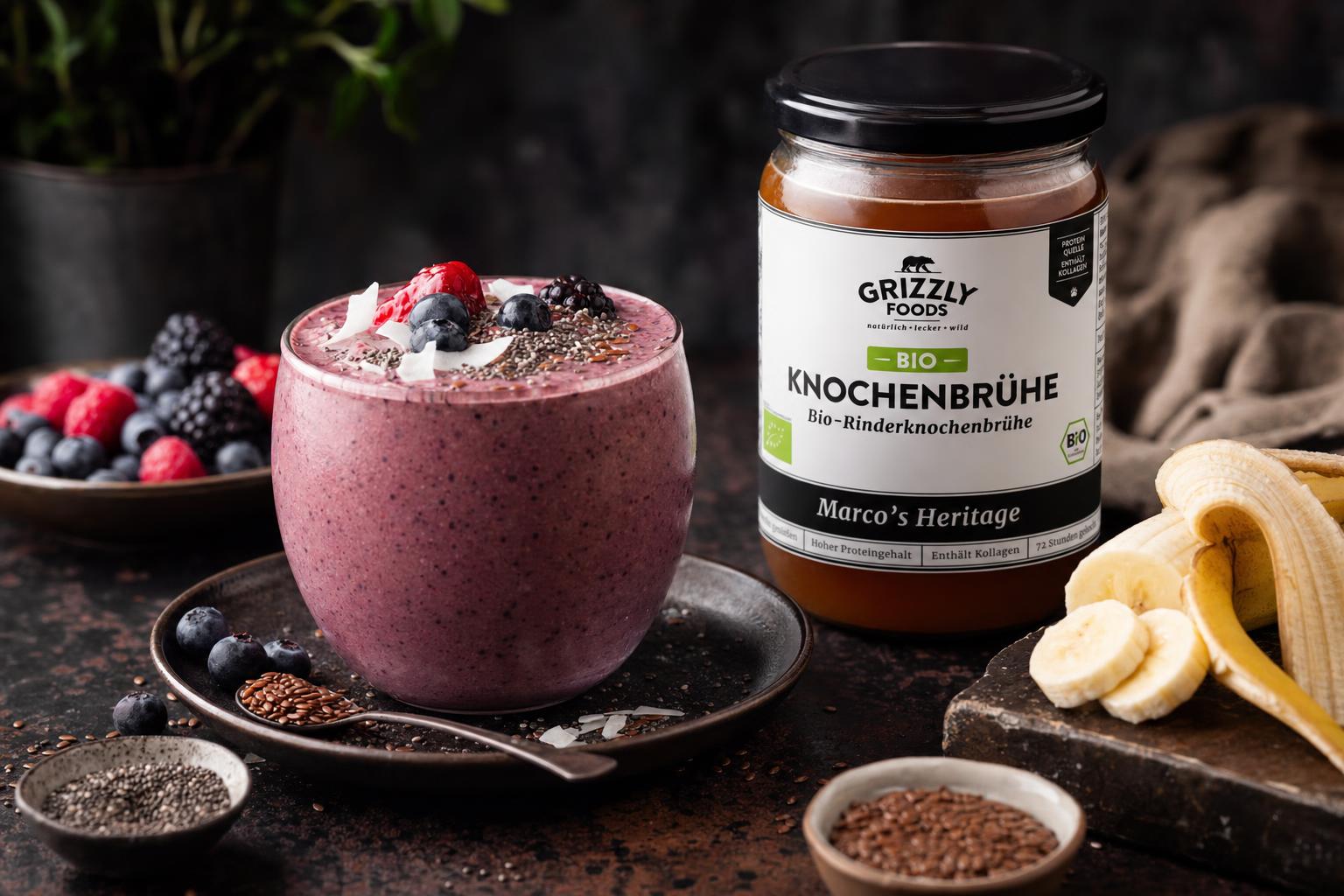 Cremiger Beeren-Smoothie in einem Glas, daneben ein Glas mit klarer Rinderknochenbrühe auf hellem Untergrund.
