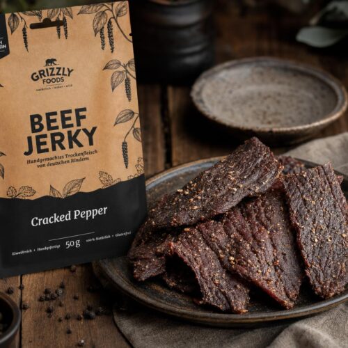 Dünne Streifen Beef Jerky auf einem Holzbrett, daneben ein geöffneter Beutel mit getrocknetem Rindfleisch.