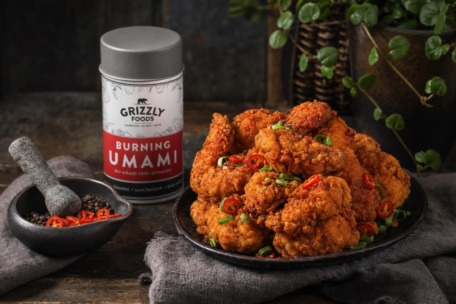 Knusprig gebratene Hähnchenteile in einer gusseisernen Pfanne, garniert mit Frühlingszwiebeln und roten Chilischoten.