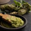 Frisch geriebener echter Wasabi mit grober, stückiger Textur auf Holzreibe, daneben ein Wasabi-Rhizom, blassgrün und frisch.