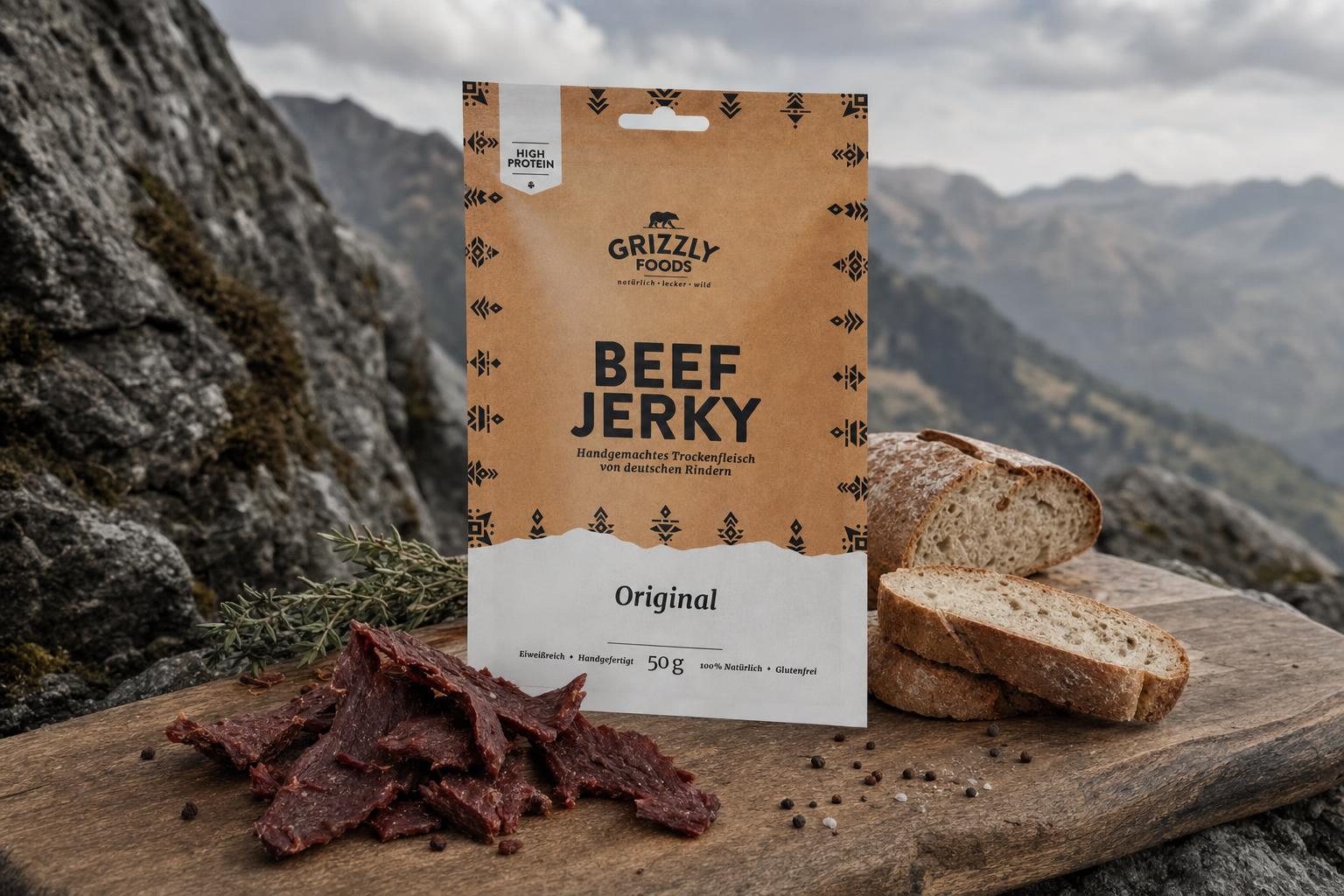 Rindfleisch-Jerky, Brotscheiben und ein Taschenmesser auf einem Holzbrett im Freien vor unscharfer Bergkulisse angerichtet