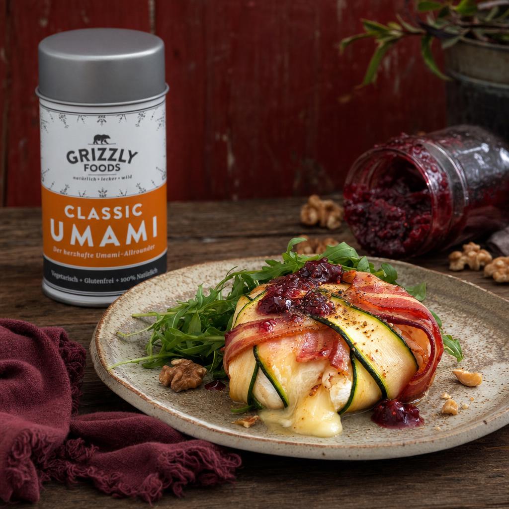 Gebackener Camembert im Zucchini-Speck-Mantel auf Teller mit Rucolasalat, Walnüssen und Klecks Beerenmarmelade, daneben Marmeladenglas.