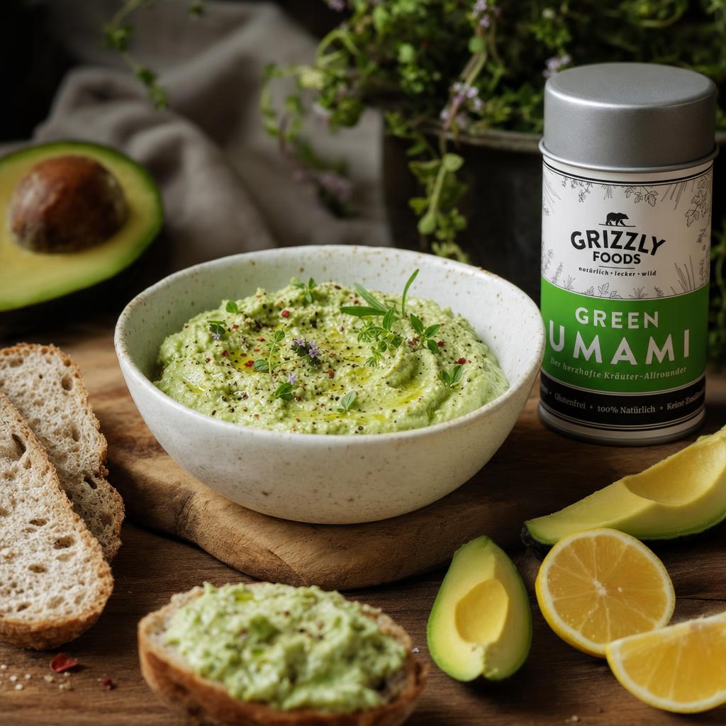 Cremiger Avocado-Dip mit frischen Kräutern in einer weißen Schale, dazu Brotscheiben, Avocadowürfel und Zitronenscheiben.
