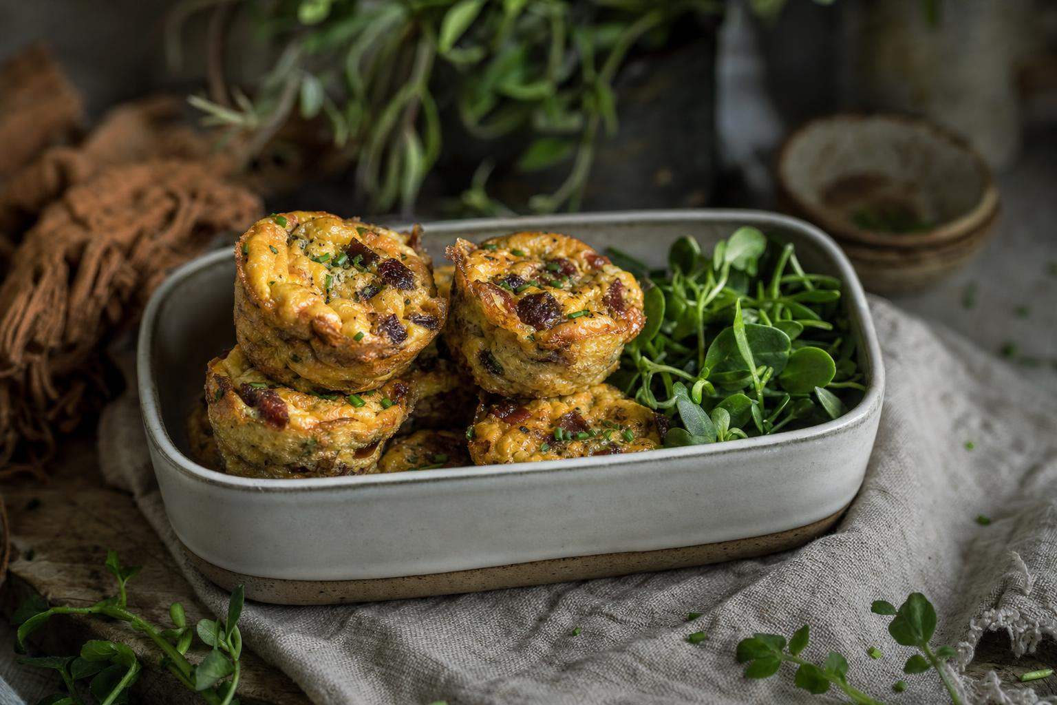 Jerky Muffins Airfryer – Mehrere herzhafte Ei-Muffins mit Kräutern gestapelt in einer Lunchbox, bereit für Meal Prep, bei natürlichem Tageslicht.