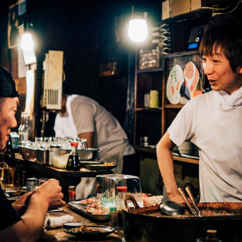 Zwei Personen, die sich an einem Streetfood Stand, an dem japanisch gegrillt wird, unterhalten