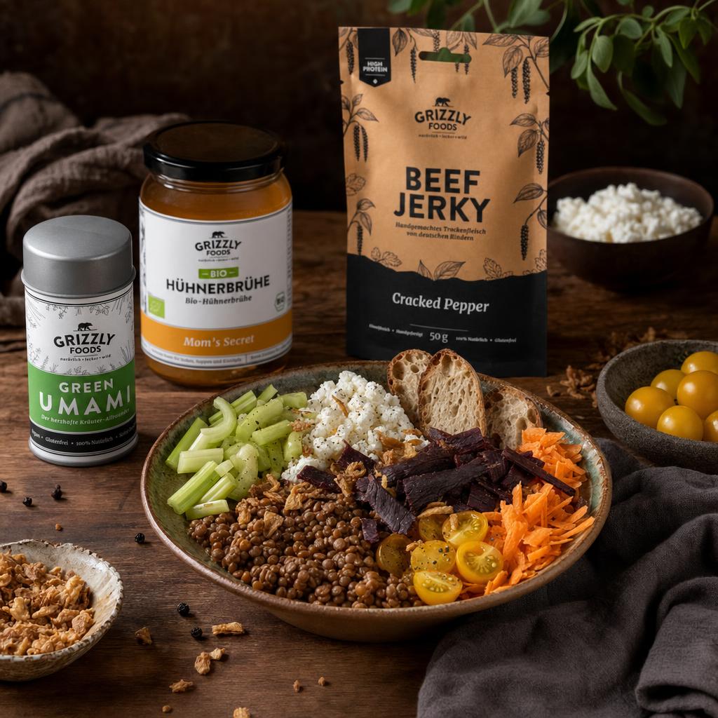 Protein Bowl mit Linsen, Hüttenkäse, frischem Gemüse, Brot und knusprigen Toppings, umgeben von Beef Jerky, Gewürzen und Kräutern