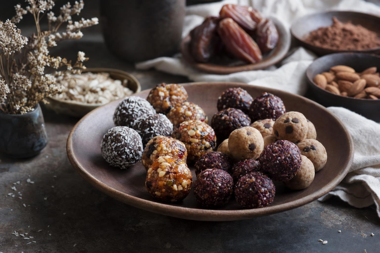 Alternativen zu Proteinriegeln – Verschiedene Snacks wie Nüsse, Trockenfrüchte, Joghurt mit Beeren und Haferflocken auf einem hellen Holztisch angerichtet.