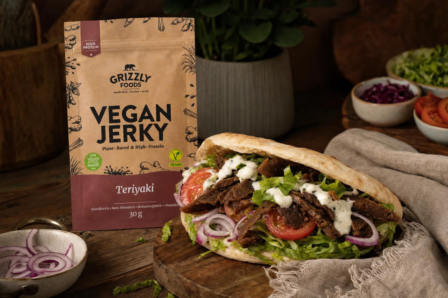 Veganer Döner im Fladenbrot mit Vegan Jerky, Salat, Tomaten, roten Zwiebeln und weißer Sauce auf Holzplatte angerichtet.