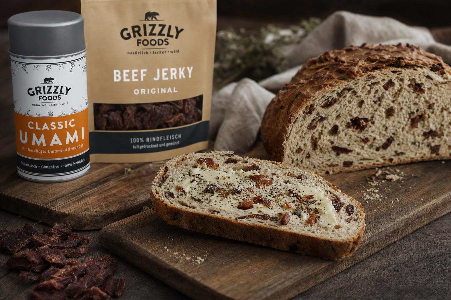 Eine Scheibe Zwiebelbrot mit Butter und Gewürzen auf Holzbrett, dahinter der restliche Laib; rustikale, gemütliche Atmosphäre.